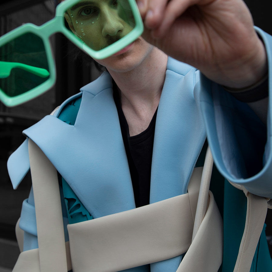 A man is dressed in a blue suit, holding sunglasses over his face