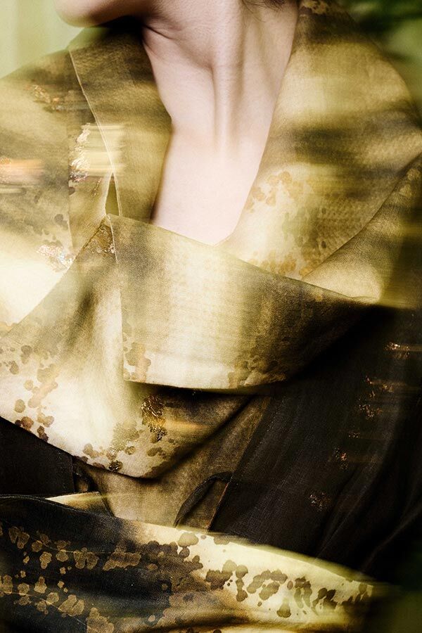 Extreme close-up of draped fabric in shades of brown, gold, and olive green, featuring a speckled and streaked metallic print.