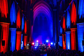 Orchestra performing in colourfully-lit church. Arches illuminated in red and blue.