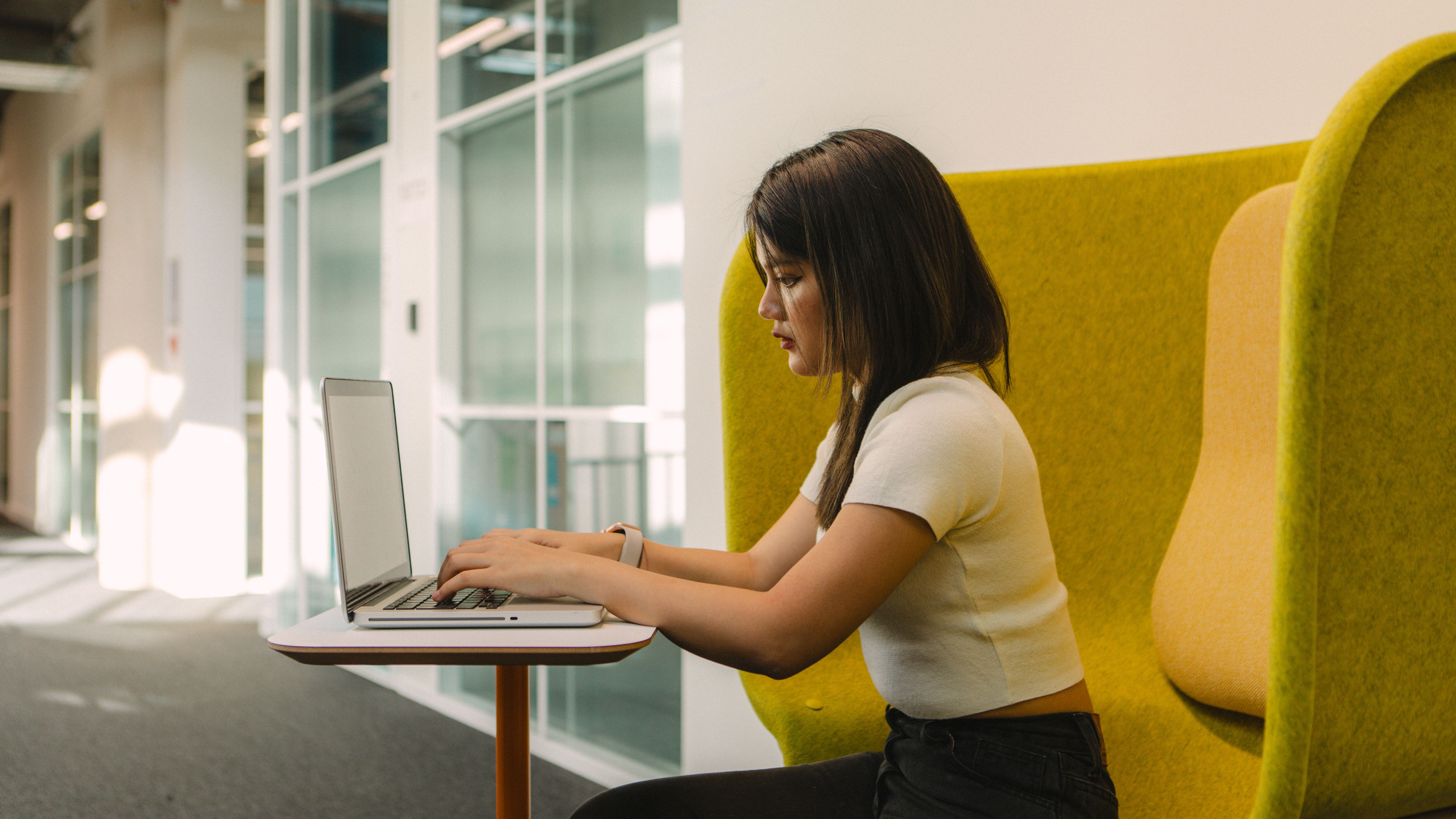 A student who appears to be female and Thai works on a laptop in a brightly coloured chair