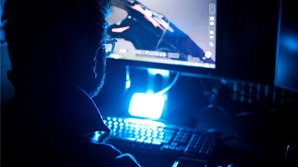 Student with glasses looking at a computer screen with blue light.