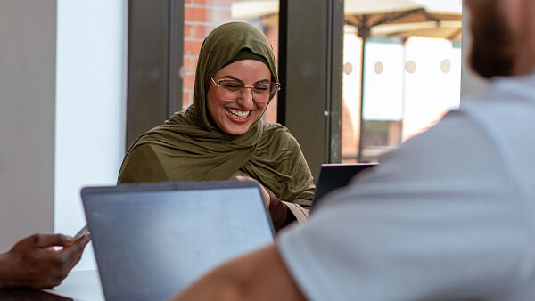 Girl in hijab laughing by laptop