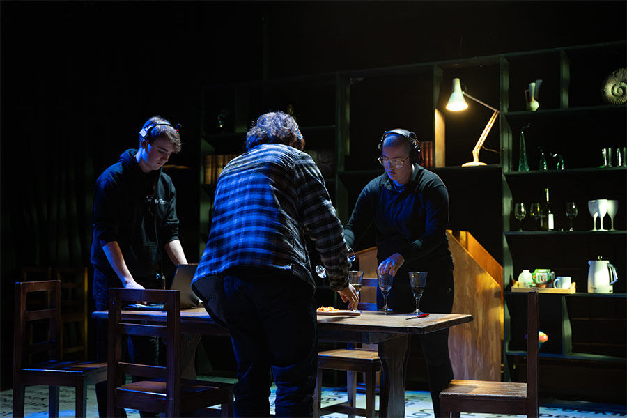 Three students are setting up a stage, placing props on a kitchen table