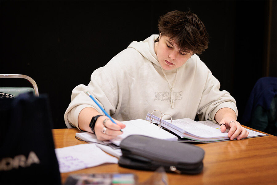 A student is sat on a table backstage, writing on a notepad