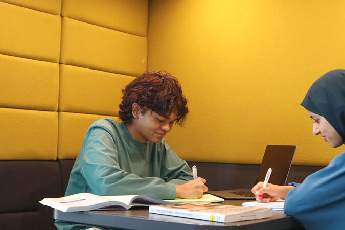 Two students writing on notepads in study booth
