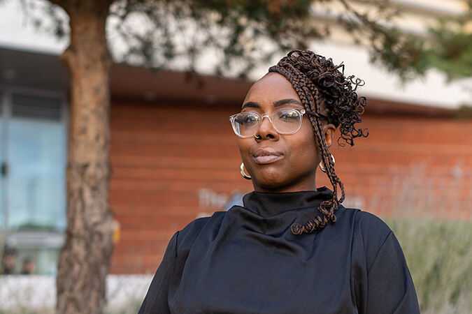 Abigail standing outside with trees in the background, she has a small smile and seems proud and confident