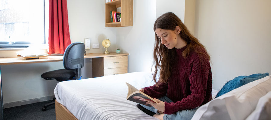 A student reads a book sitting on her bed in student accommodation