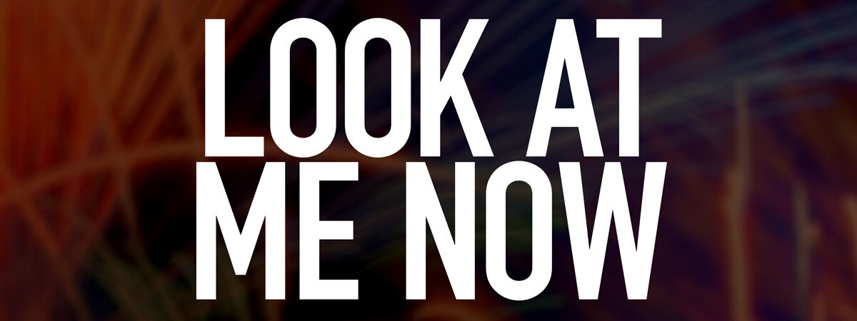 The words 'LOOK AT ME NOW' in white across a dark background.