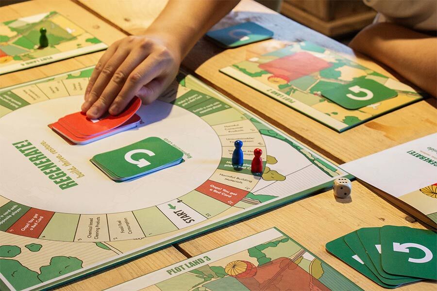 A person playing a board game called "Regenerate!" Game board has circular design with a green "G" in centre, related to sustainability