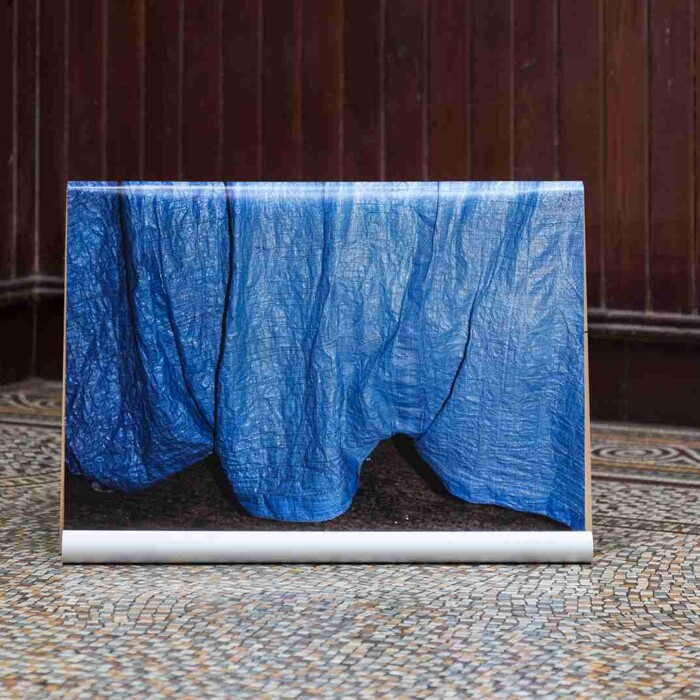 A blue draped fabric on a white stand, positioned against a dark panelled wall and a patterned floor