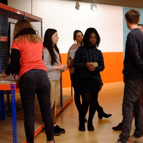 Students stood by gallery display with art on a caged structure