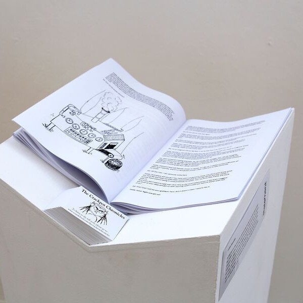 Open book with black and white illustrations displayed on a white, geometric pedestal against a neutral background