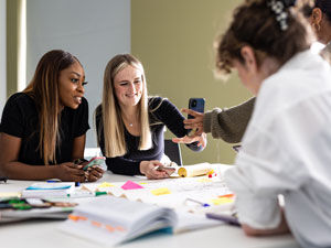 Students look at their mobile phone and smile instead of looking at the work on the desk