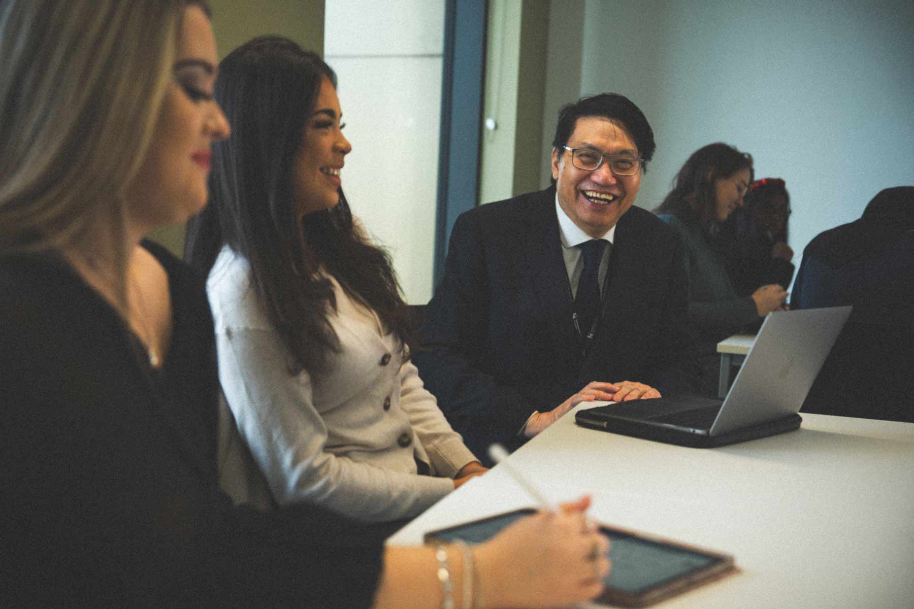 Two female students and a male lecturer, who appears to be Chinese and is wearing glasses, smiling during a teaching session