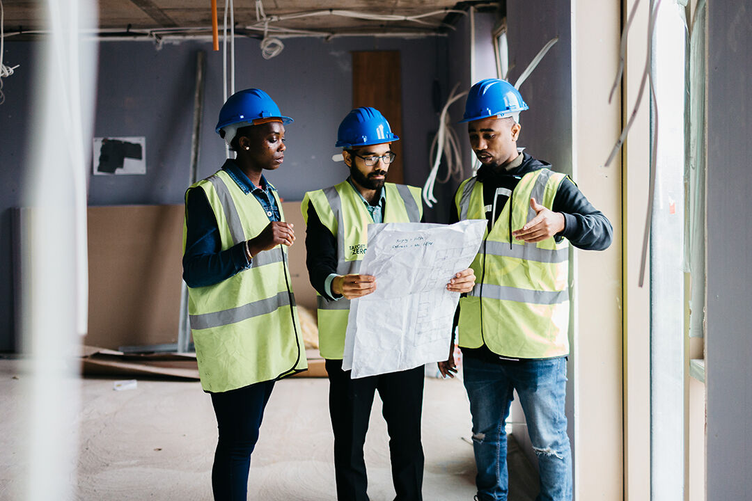 Three students on construction site, one holding a blueprint