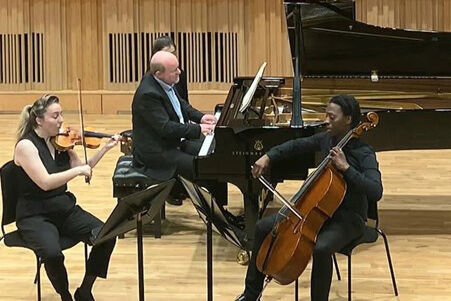 A celloist, violinist and pianist performing on stage