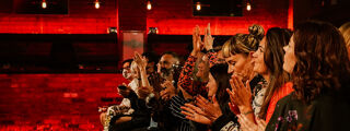 An audience looks towards the stage and applauds