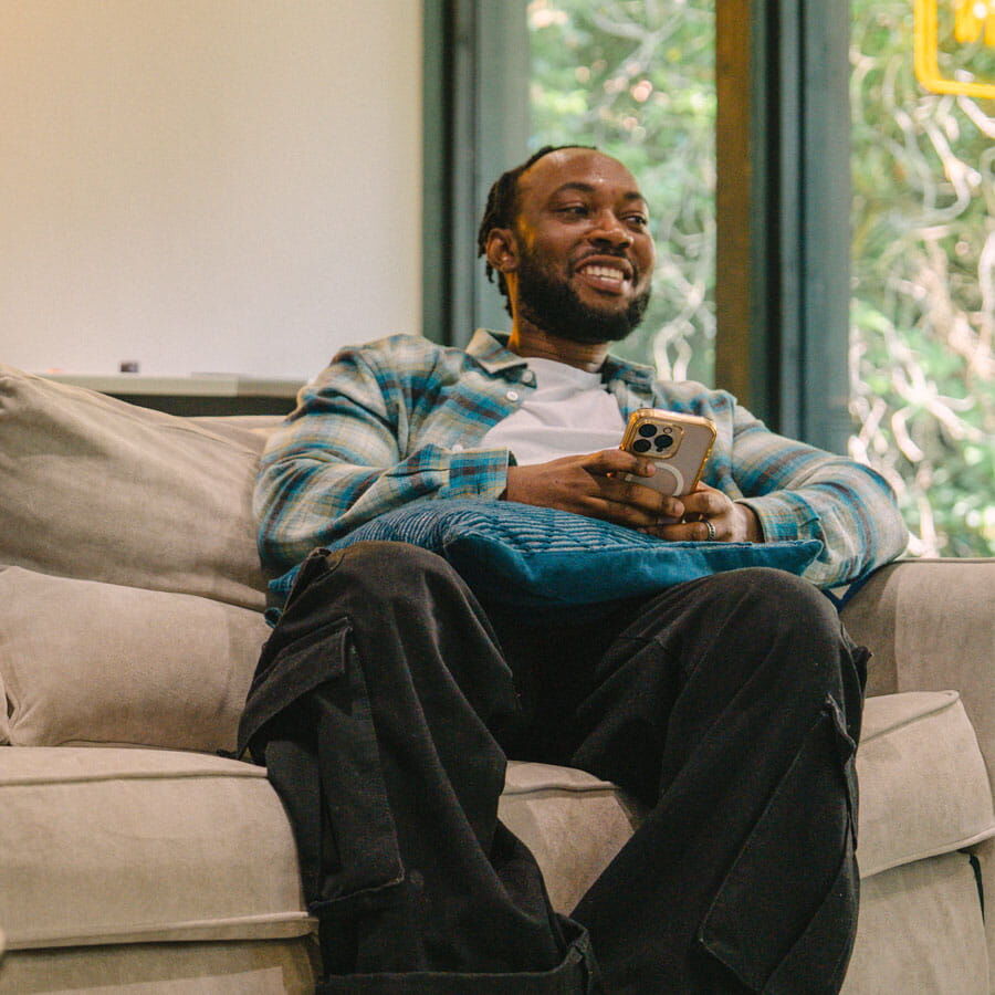 A student sits and smiles while relaxing at home in modern, bright and spacious University accommodation
