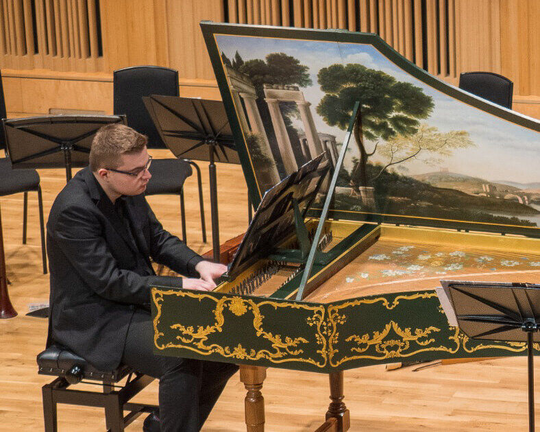 Student playing an ornate early style piano