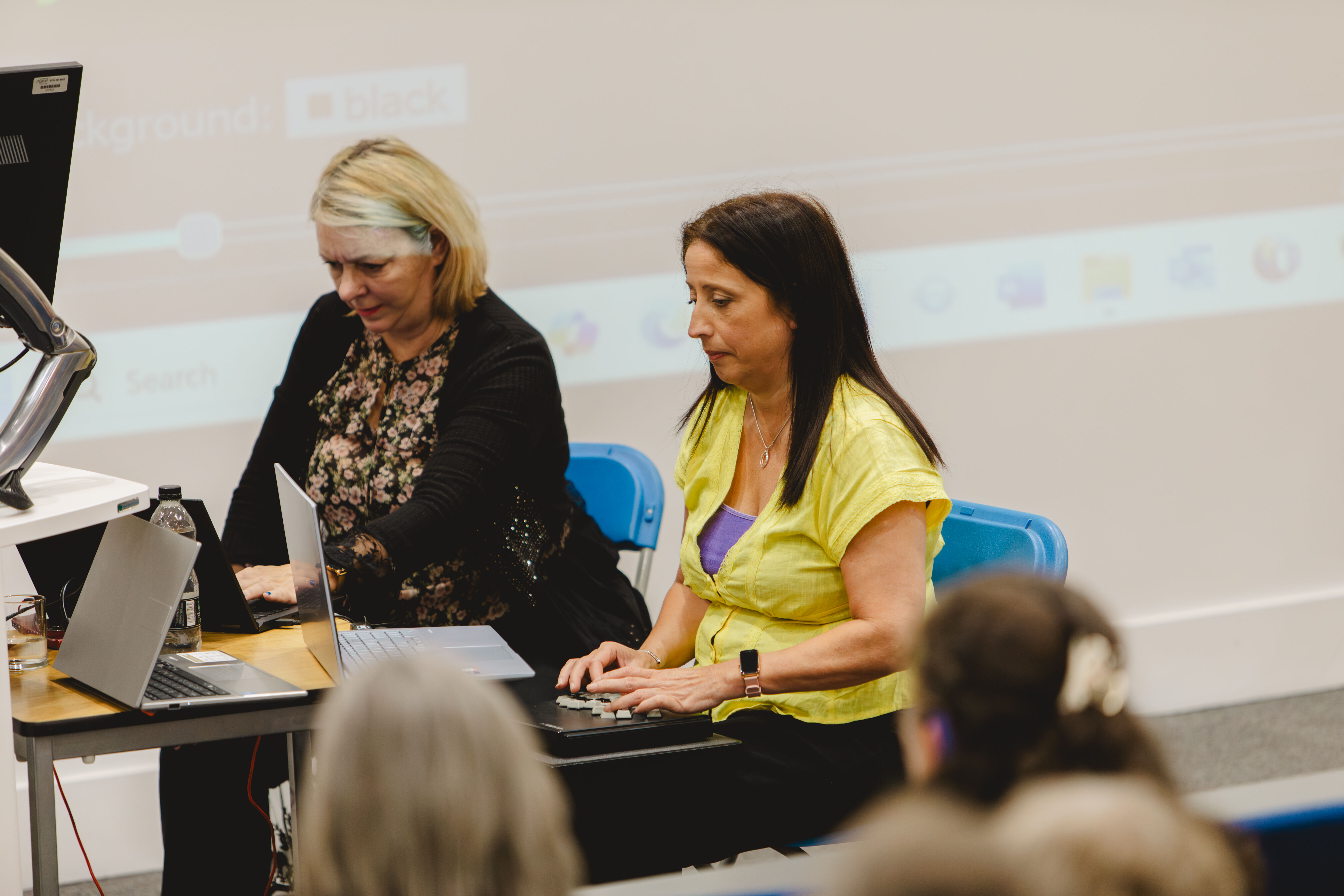 Two ladies one with blonde hair and one with dark hair type on transcribers 