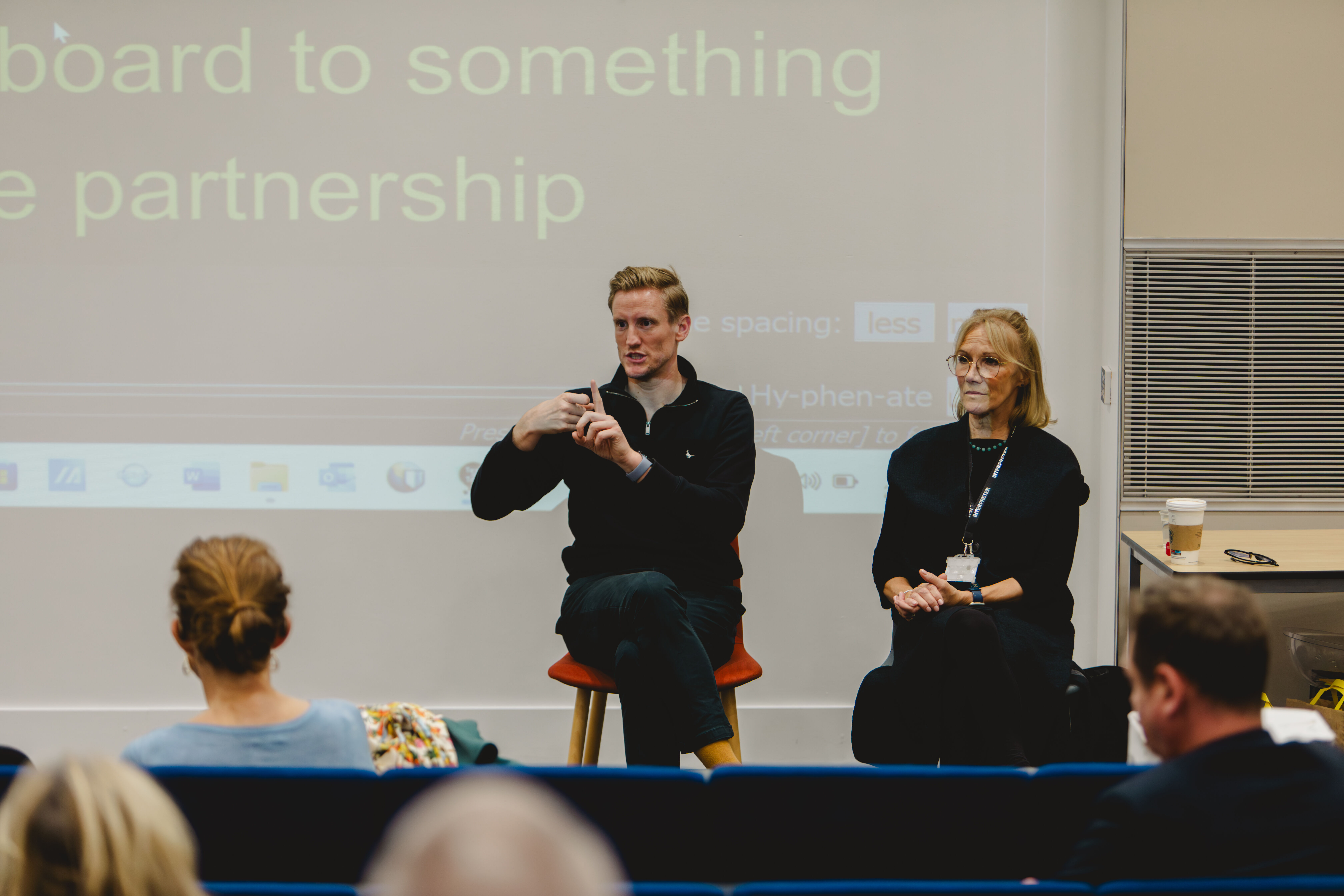 A man and a lady with blonde hair sign to the audience