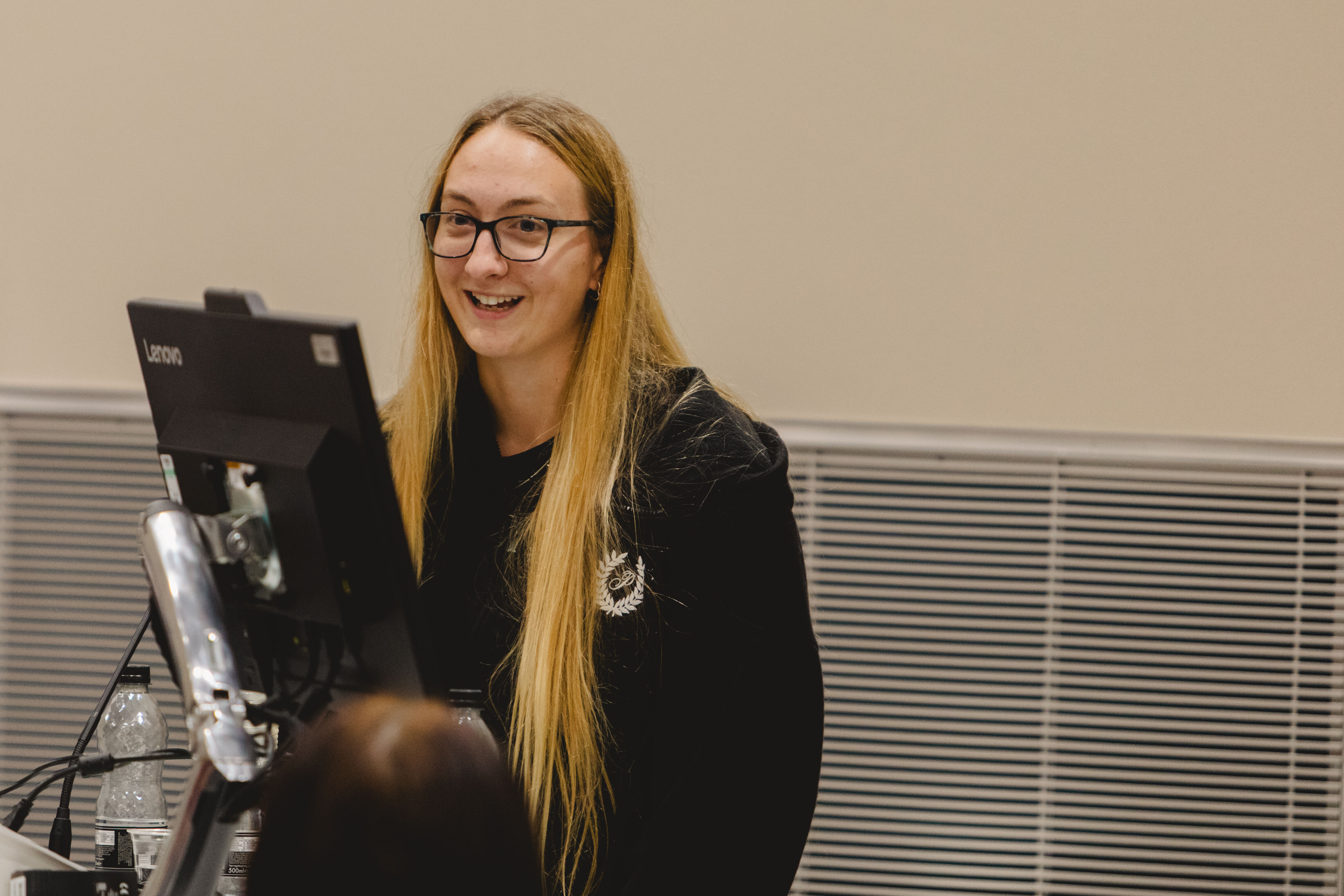 A girl with long blonde hair speaks to the audience at a computer