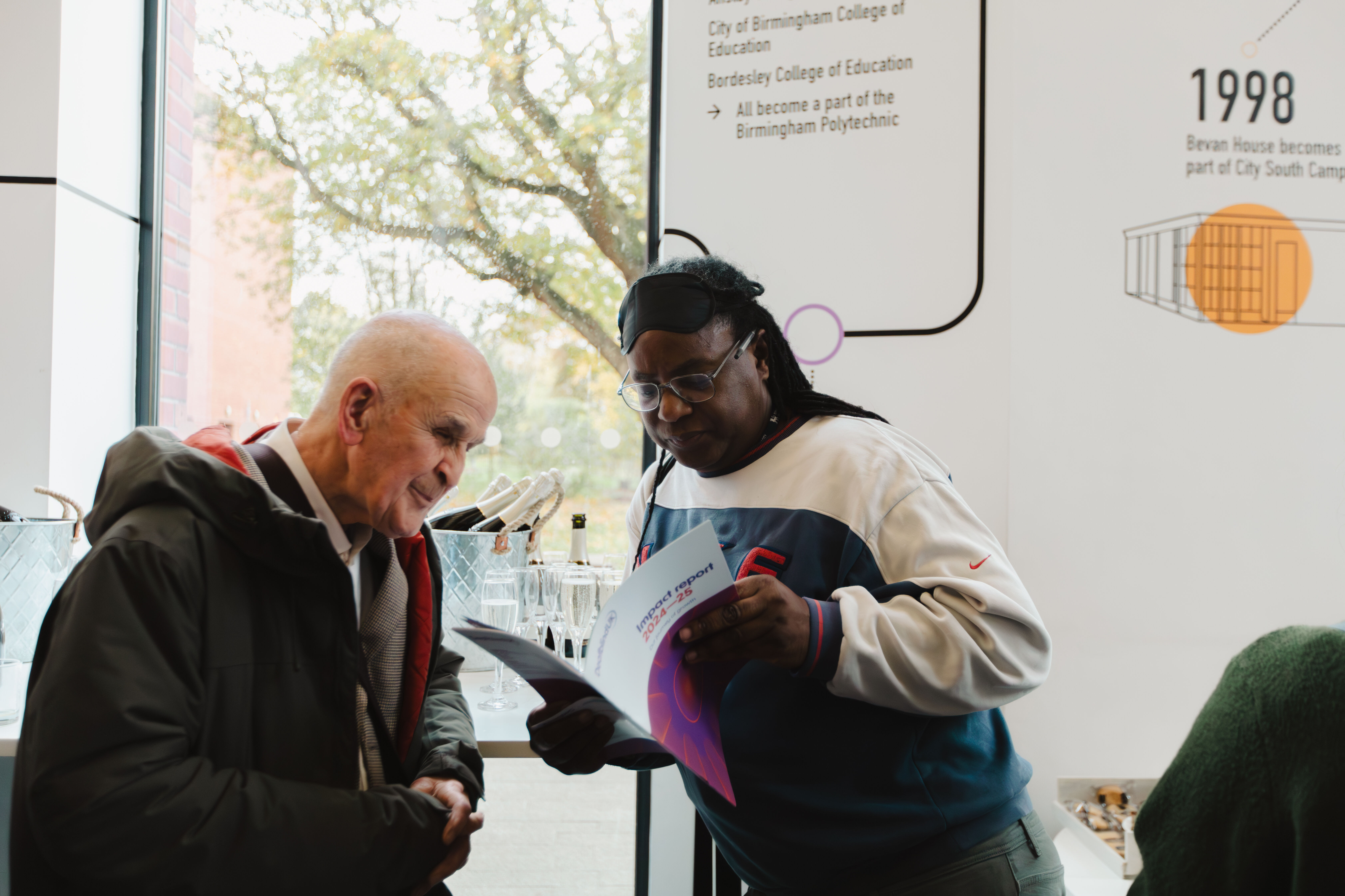 Two men stand together reading an impact report of Deafblind UK