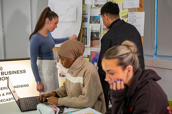 Four young people working together on a project with a laptop and papers.