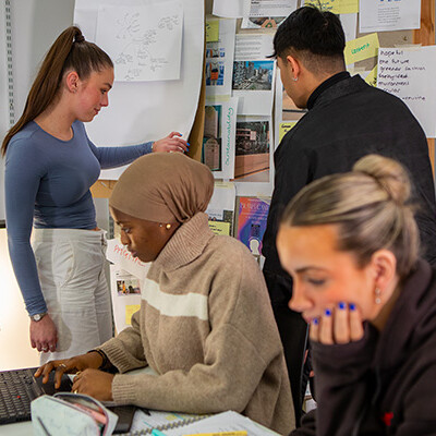 Four young people working together on a project with a laptop and papers.