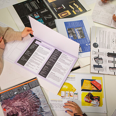 A group of young people are sitting around a table, looking at different papers and notebooks. It looks like they're working on a school project together!
