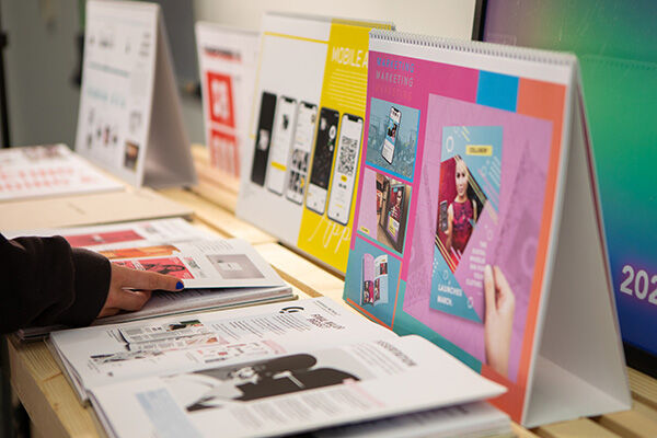 A person is looking through a collection of cool-looking brochures and booklets displayed on a table. It seems like they might be checking out different designs or projects!