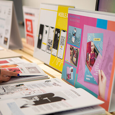 A person is looking through a collection of cool-looking brochures and booklets displayed on a table. It seems like they might be checking out different designs or projects!