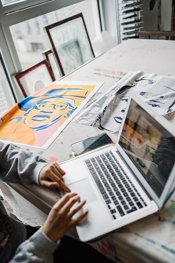 Student at laptop next to textile artwork samples of portraits