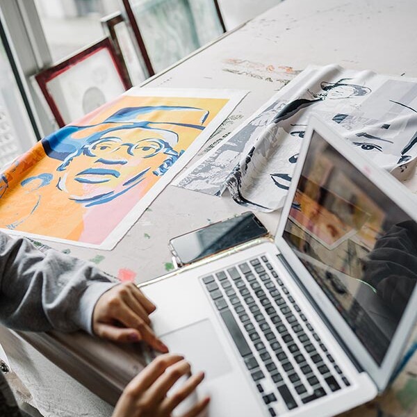 Student at laptop next to textile artwork samples of portraits