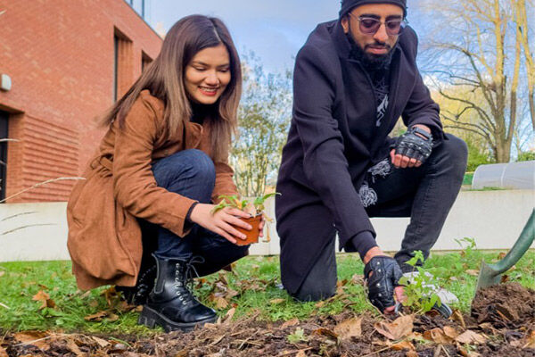 Two students gardening, holding a plant pot each