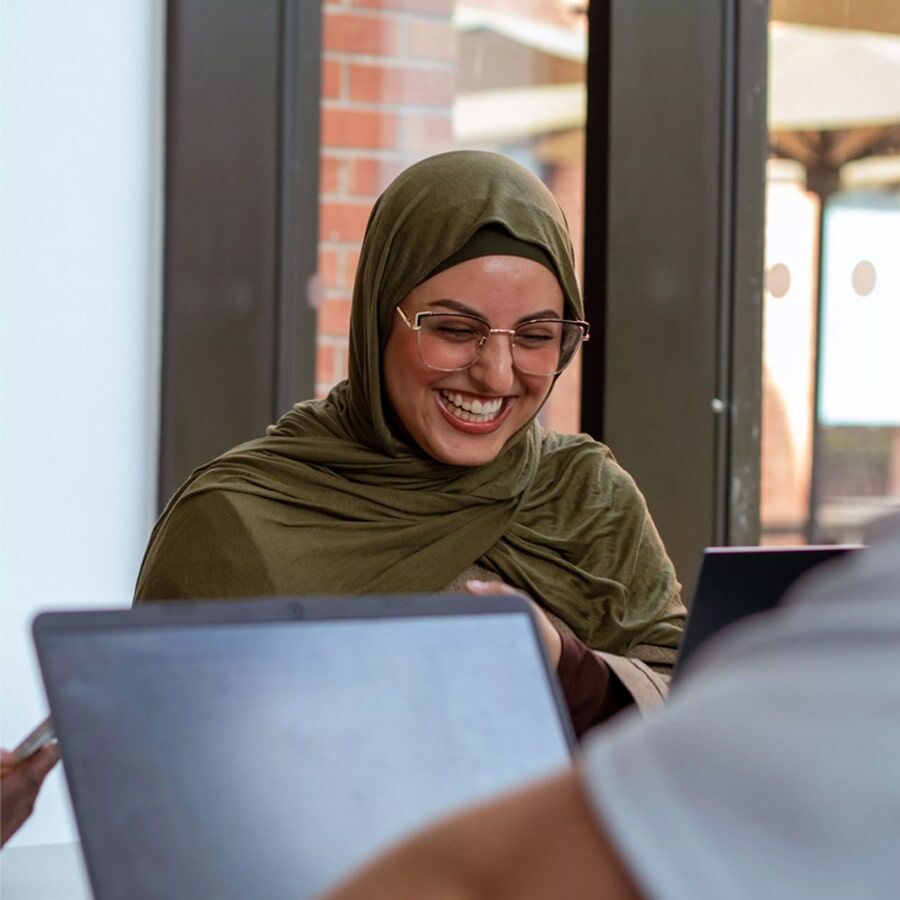 A picture of a happy student, sitting at a computer and laughing