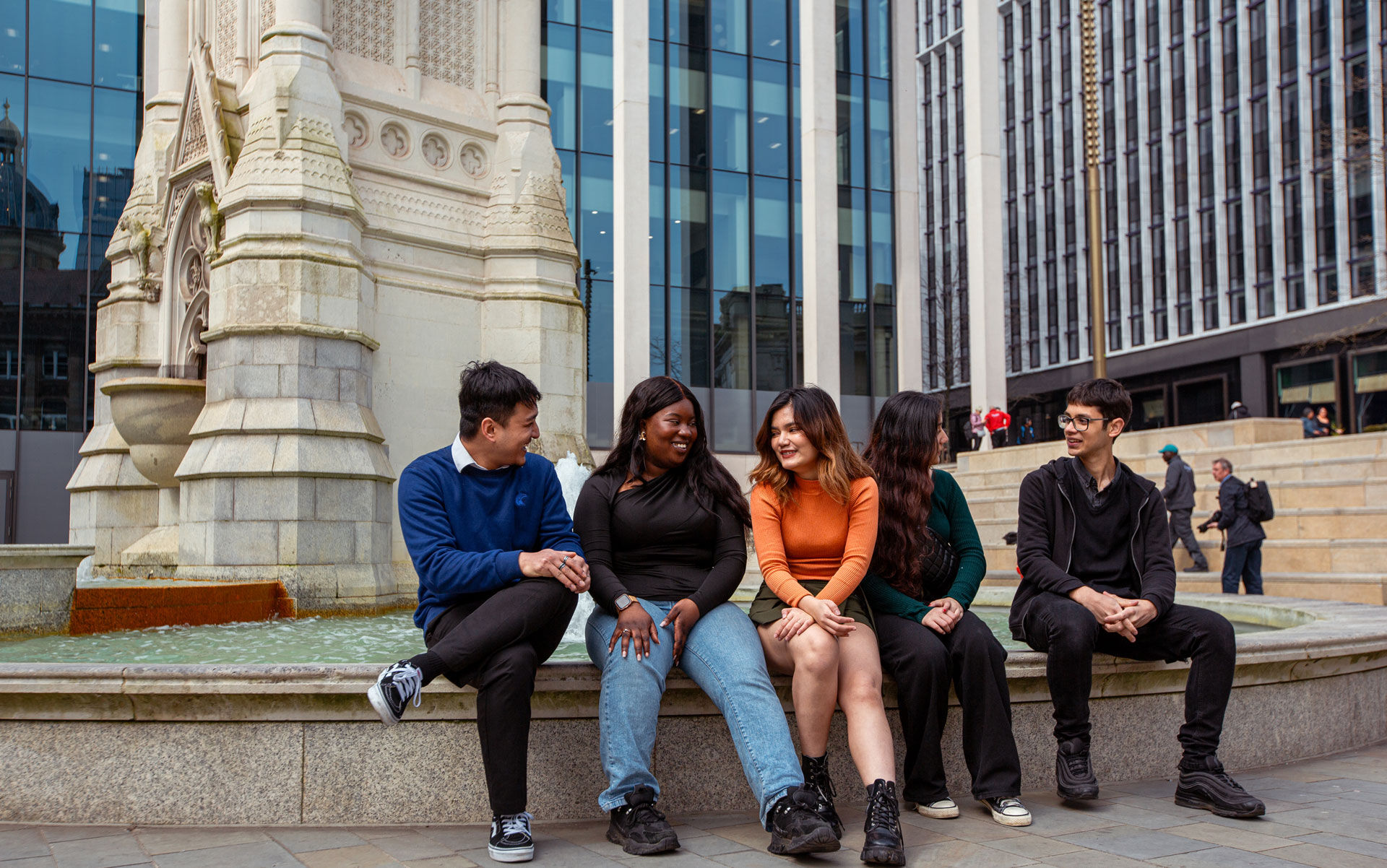 Five students talk sitting by a fountain in Birmingham City Centre