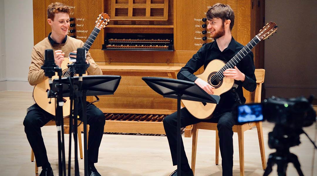 Two students holding guitars with music sheets in front of them