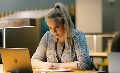 Student looking at laptop and writing in notebook.