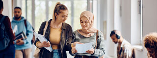 Two students walk through a university corridor and look at their exam results smiling.