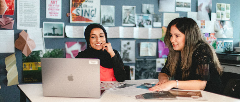 A student looks at her work on a laptop with their tutor