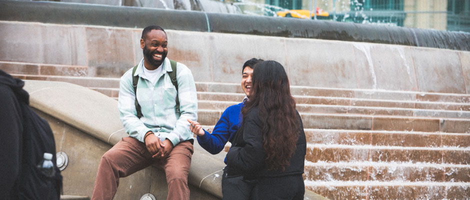 Three students laugh and talk next to a fountain in Birmingham city centre