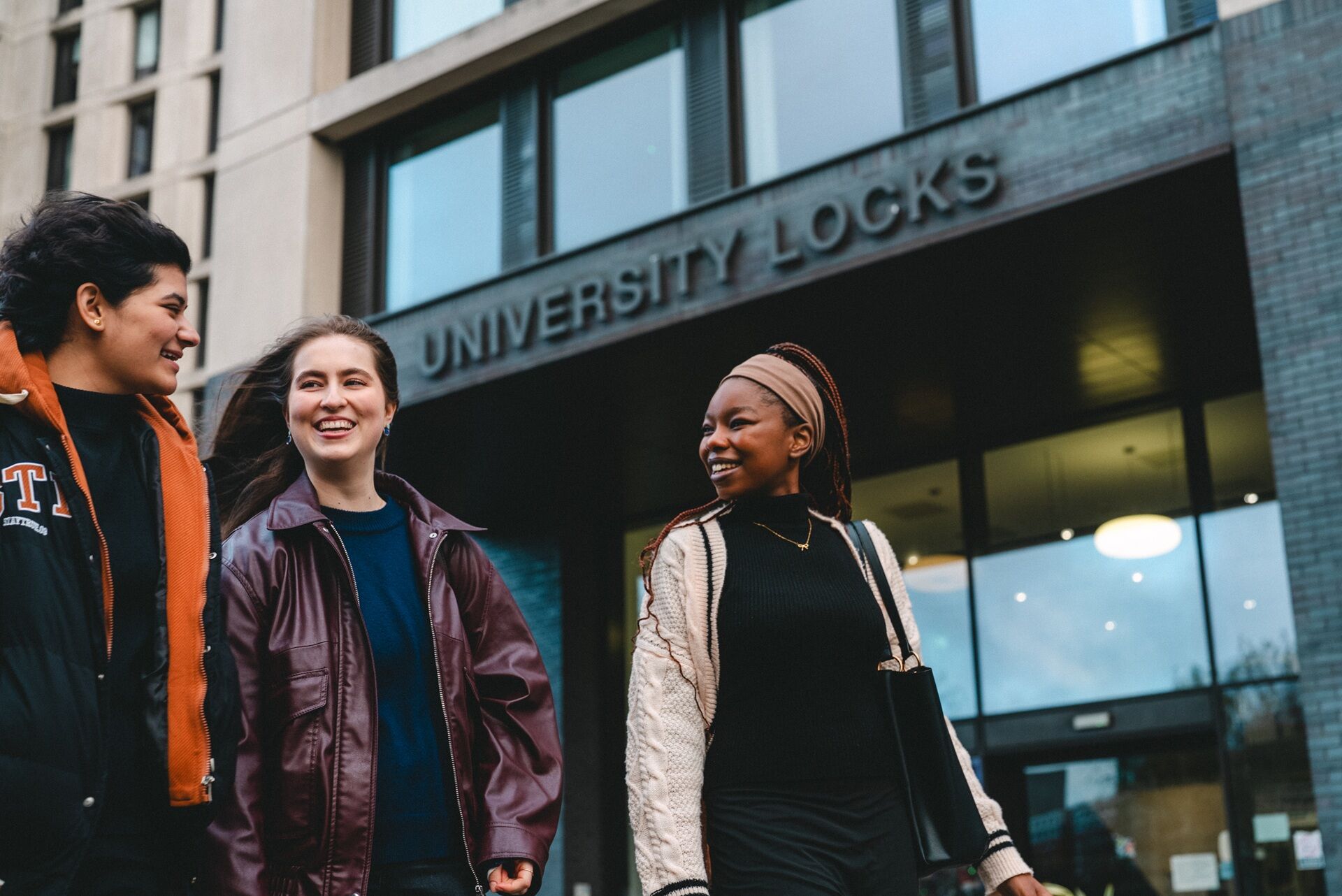 Three female students walking outside university locks student accommodation. They look happy.
