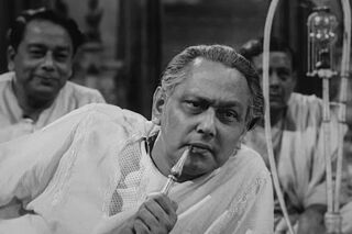 Scene from Indian film Jalsaghar, man reclining smoking sheesha