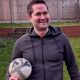 Jamie Suttle smiling, stood outside holding a football