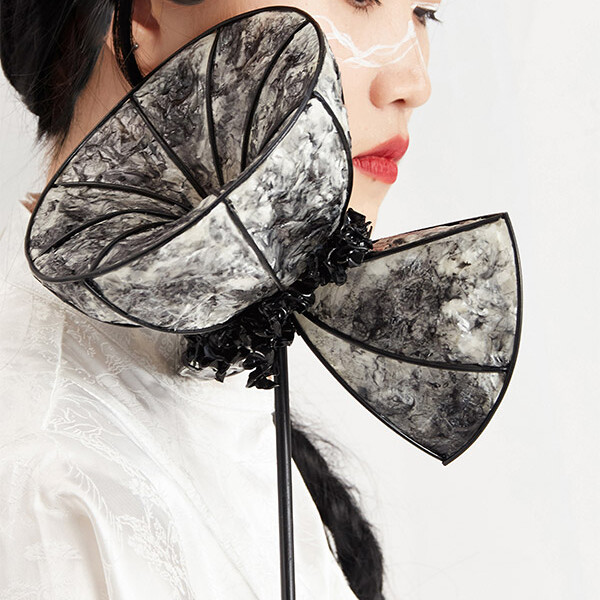 A student holding a piece of jewellery to their neck which resembles a black and white flower