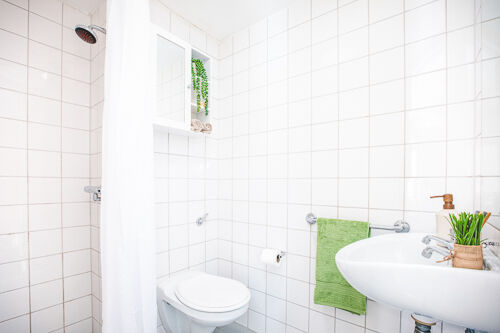 An en-suite bathroom in Lakeside student accommodation. It's a small private bathroom with a shower and shower curtain, toilet and sink. The tiles are bright white making it look very clean