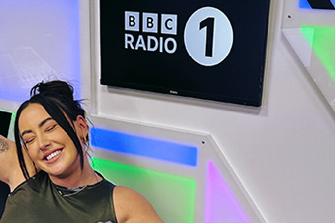 Media Production student, Lauren Donlevy, posting with the Radio 1 logo in the radio studios.