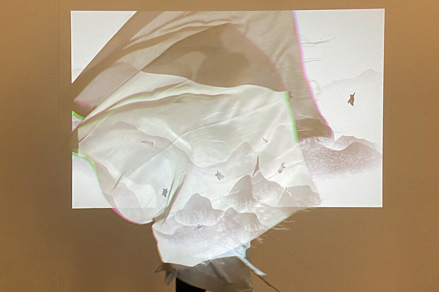A translucent fabric draped over a wall. It is backlit by a projector, casting a projected image of a serene landscape onto the fabric