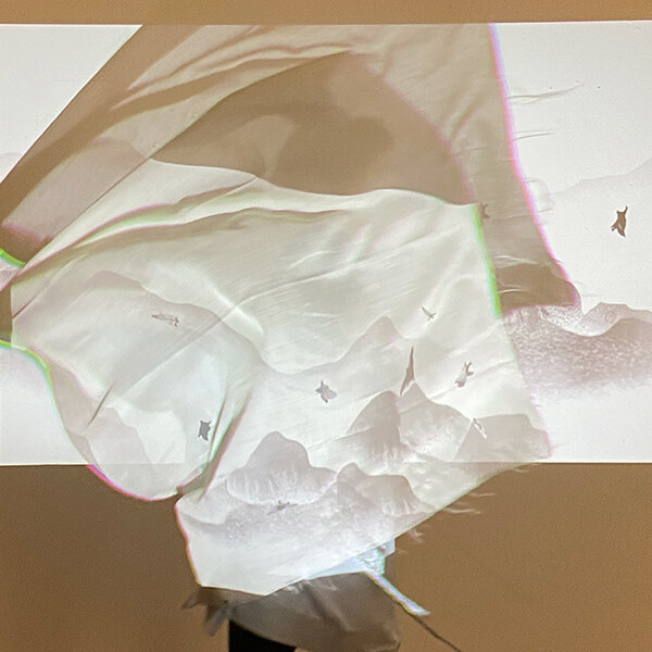 A translucent fabric draped over a wall. It is backlit by a projector, casting a projected image of a serene landscape onto the fabric